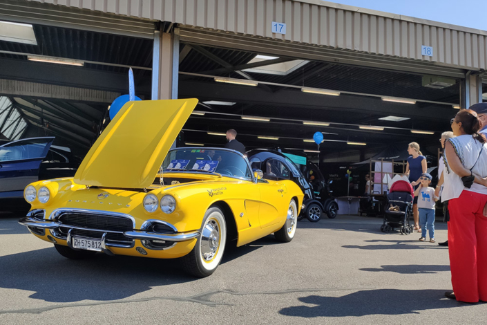 Eine gelbe Corvette Jahrgang 1962 steht mit offener Motorenhaube vor einer Halle.