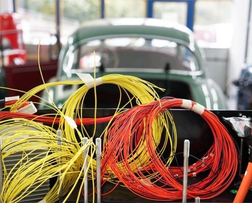 Gelbe und rote Kabel, zusammengerollt, die aus der Batteriebox herausschauen. Im Hintergrund das Fahrzeug, in welches die Batteriebox eingebaut wird.