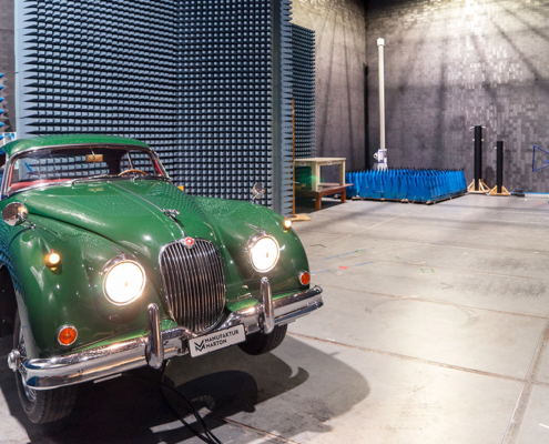 Jaguar XK150 in einer Prüfhalle. Die Prüfhalle ist mit Absorbern ausgestattet, im Hintergrund sieht man die Antenne, welche die elektromagnetischen Strahlen misst.