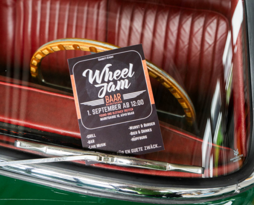 Ein Flyer für das Young- und Oldtimer-Treffen "Wheel Jam" ist am Scheibenwischer unseres Jaguar XK 150 eingeklemmt. Im Hintergrund Lenkrad und Sitze, durch die Frontscheibe hindurch gesehen