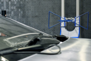 Ein DeLorean wird gerade auf seine elektromagnetische Verträglichkeit geprüft. Er steht in einer Prüfhalle, eine blaue Antenne ist auf ihn gerichtet und misst seine elektromagnetischen Strahlungswerte. Man sieht im Bild Teile der Frontscheibe sowie der Fronthaube, ein Kabel, und im Hintergrund eine auf das Fahrzeug gerichtete Antenne