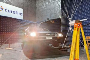 Ein DeLorean wird gerade auf seine elektromagnetische Verträglichkeit geprüft. Er steht in einer Prüfhalle, eine Antenne auf gelbem Stativ ist auf ihn gerichtet und emittiert Strahlung, um seine Immunität zu testen.