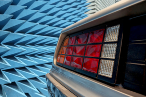Ein Teil des Hecks des DeLoreans in einer Prüfhalle für elektromagnetische Immunität. Im Hintergrund die Wand der Halle, an der blaue Pyramidenabsorber angebracht sind.