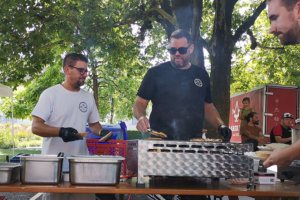 Zwei Männer am Grillstand. Einer wendet gerade ein Burger Patty.