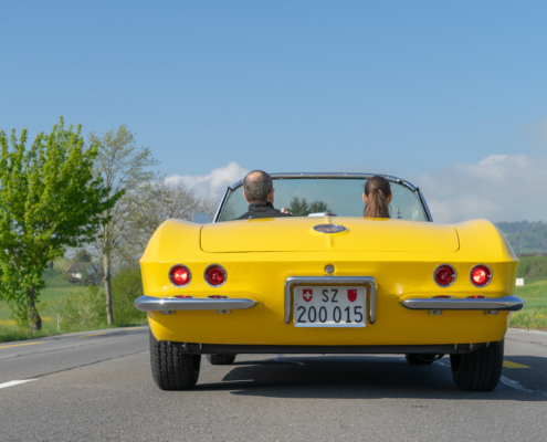 View of a Corvette driving away from the rear with two occupants.
