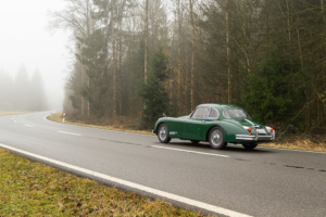 Electric Jaguar XK150 driving on a misty country road.