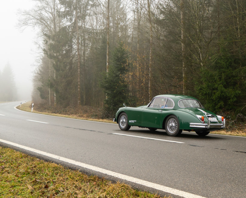Electric Jaguar XK150 driving on a misty country road.