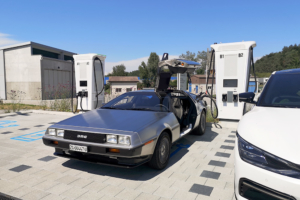 Delorean wird an der Ladesäule geladen. Ansicht des ganzen Fahrzeugs, leicht schräg.
