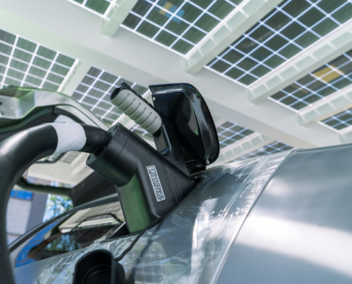 DSC05873_manufakturmarton_ladedose_blog Detailaufnahme. Die offene Ladeklappe, mit eingestecktem CCS-Stecker, von unten aufgenommen. Im Hintergrund das Solardach der Ladestation.