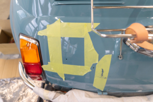 Die Heckklappe des Fiat 500 in mittelblau. Die Stelle, an die künftig die Ladeklappe kommen soll, ist mit Malerklebeband markiert.