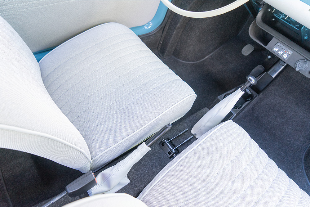 The colour and material scheme for the interior was also implemented in accordance with the customer’s wishes Car seats upholstered in light-coloured fabric, viewed from above. In between are various levers: the handbrake, the temperature control and the gear lever.