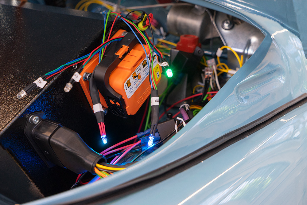 Preparations and testing of the LEDs to be fitted in the display The front compartment of a vehicle. Various cables are visible, some of which have LEDs of different colours fitted. An orange manual safety disconnect switch is fitted to a black box, the battery box.