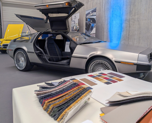 manufakturmarton_SCW2026_20260529_124821686 Ein Tisch mit Stoffmustern, im Hintergrund der DeLorean