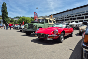 Aufgereihte Fahrzeuge am Fahrzeugmarkt, im Fokus auf dem Bild ein roter Jaguar E-Type, dahinter ein olivgrüner Landrover
