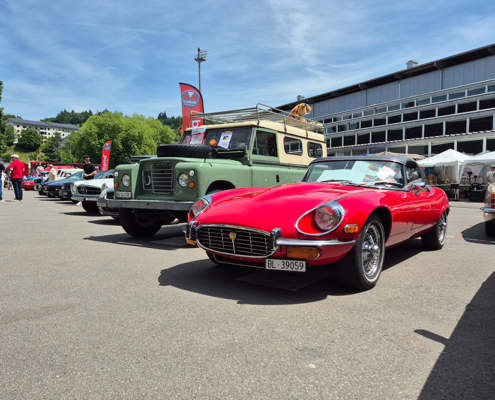 manufakturmarton_SCW2026_20260530_140223 Aufgereihte Fahrzeuge am Fahrzeugmarkt, im Fokus auf dem Bild ein roter Jaguar E-Type, dahinter ein olivgrüner Landrover