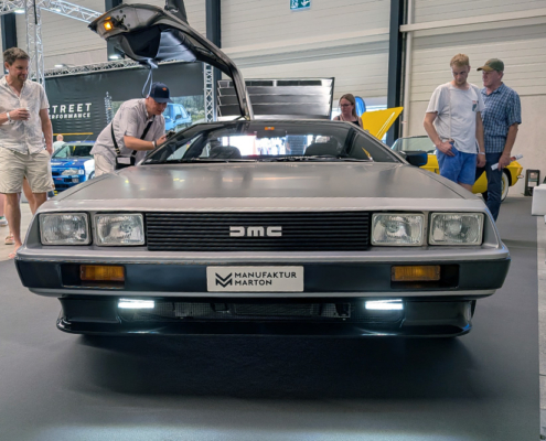 manufakturmarton_SCW2026_20260531_130830241 Der DeLorean von vorne. Es stehen Leute um das Fahrzeug und betrachten es.